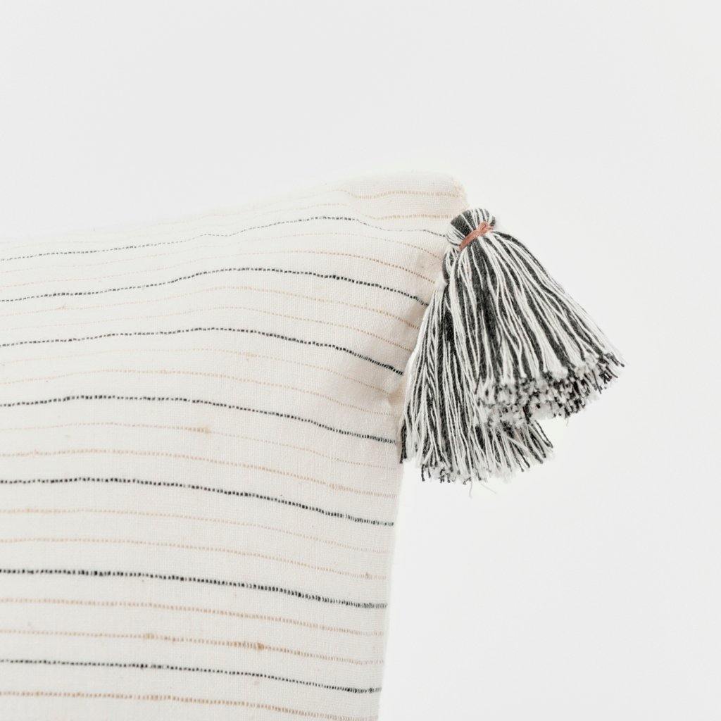 A soft ivory pillow in 22x22 inch size featuring fawn and indigo striped weave and lush corner tassels.