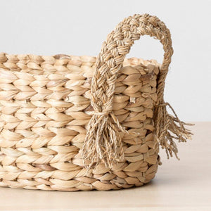 Closeup view of a dried water grass basket in a buttery golden hue, finished with braided handles. Perfect to stash fruits, towels, candles etc.  