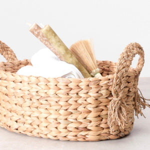 Closeup view of a dried water grass basket in a buttery golden hue, finished with braided handles. Perfect to stash fruits, towels, candles etc.  